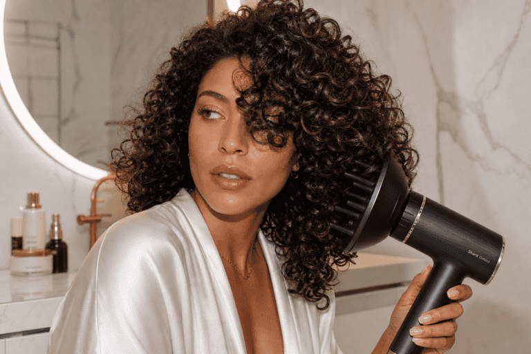 Woman with curly hair using a Shark hair dryer with diffuser attachment in a marble bathroom
